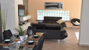 A modern living room with a glass dining table, black sofas, and a TV mounted on the wall. - Villa with Private Pool, Terrace, A/C and Wi-Fi (San Miguel de Salinas)