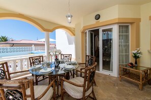 A covered outdoor dining area with a glass table, wicker chairs, and a view of the ocean. - Pet-Friendly Villa Encantada with Sea View & Pool (Arona)