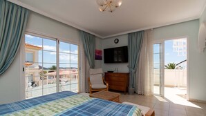 A bedroom with a bed, a TV, a chair, a small table, and a balcony with a view. - Pet-Friendly Villa Encantada with Sea View & Pool (Arona)