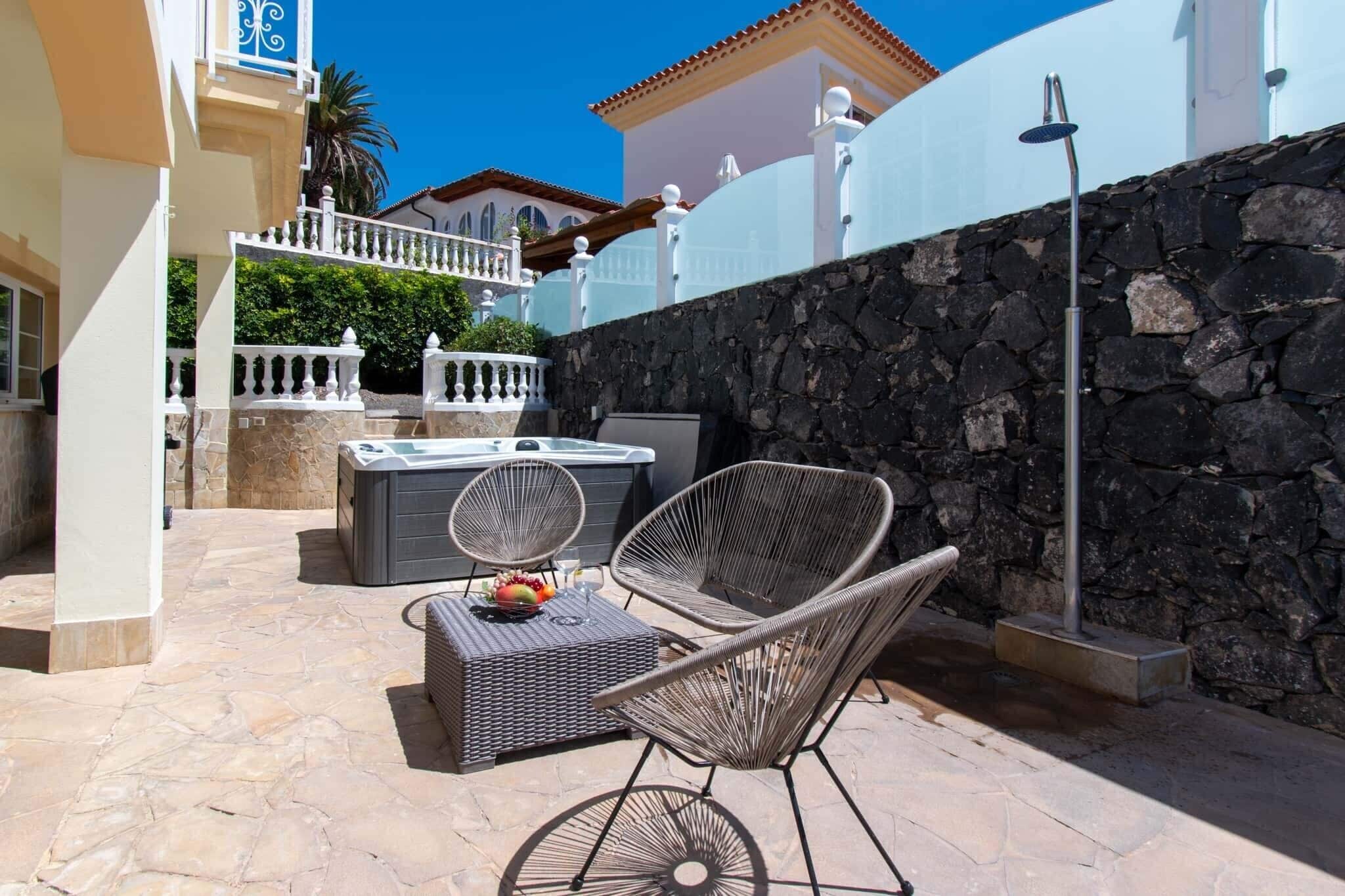 Une terrasse extérieure avec un sol en pierre, des meubles en osier, un jacuzzi et un mur en pierre.