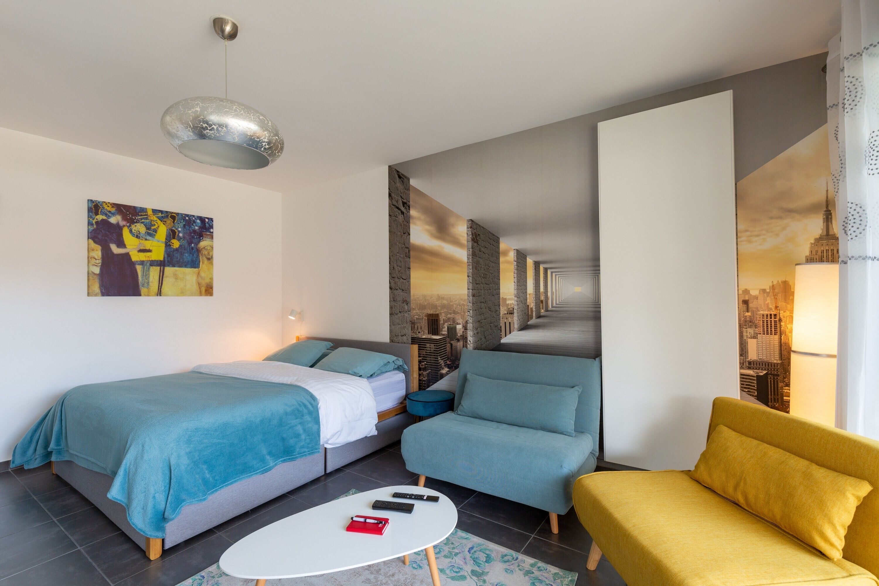 Ein modernes Hotelzimmer mit einem Bett, zwei Sofas, einem kleinen Tisch und einer Stadtansicht als Wandgemälde.