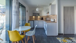 A modern kitchen with a dining area, a washing machine, and a view through a glass door. - 'Grand Studio by the Lake' with Mountain Views, Terrace and Wi-Fi. (Saint-Jorioz)