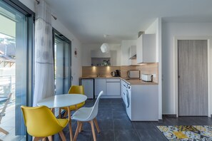 A modern kitchen with a dining area, a washing machine, and a view through a glass door.