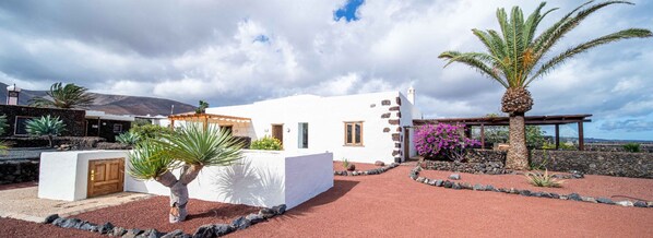 A white building with a stone facade, a palm tree, and a rock garden.