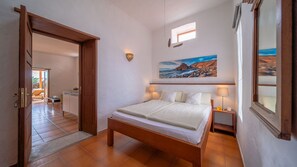 A bedroom with a wooden bed, a painting of a coastal scene, and a view of a balcony.