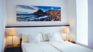 Een hotelkamer met een bed, twee bedlampen, een nachtkastje met een bloem en een schilderij van een kustlandschap.