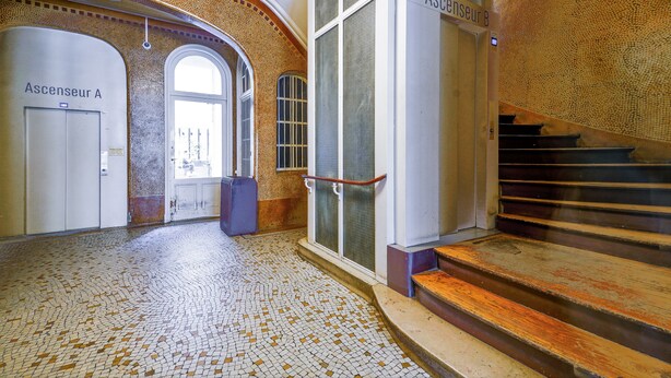Ein gefliester Boden, eine Treppe und zwei Türen mit der Aufschrift 'Ascenseur A' und 'Ascenseur B'.