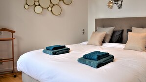 Ein ordentlich gemachtes Bett mit zwei gefalteten Handtüchern, einem Holzstuhl und einem an der Wand befestigten Spiegel.