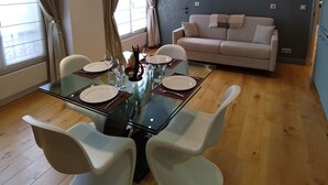 Ein modernes Wohnzimmer mit einem Glastisch, weißen Stühlen, einem beigen Sofa und einer blauen Akzentwand.