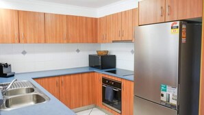 Eine Küche mit Holzausstattung, einem Edelstahlkühlschrank, einer Mikrowelle und einem Einbauofen.