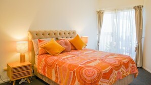 Ein Schlafzimmer mit einer geblümten Kopfteilpolsterung, einer orangefarbenen Bettdecke mit Muster und einer Nachttischlampe.