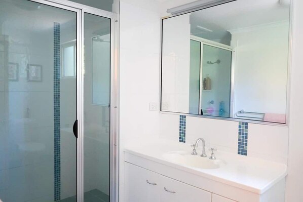 Une salle de bain avec une douche à parois de verre, un lavabo blanc avec un miroir au-dessus et un mur recouvert de carreaux.