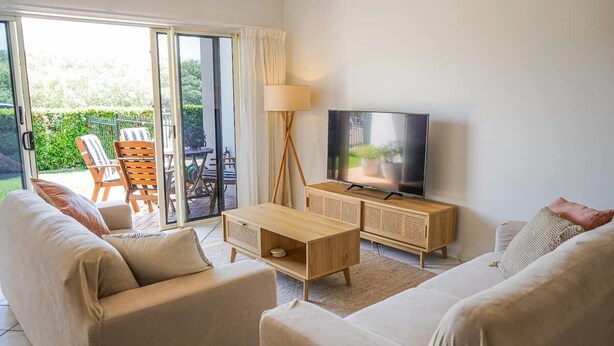 Ein Wohnzimmer mit einer Couch, einem Couchtisch, einem Fernseher und einer Schiebetür zu einem Außenbereich mit einem Stuhl und einem Tisch.