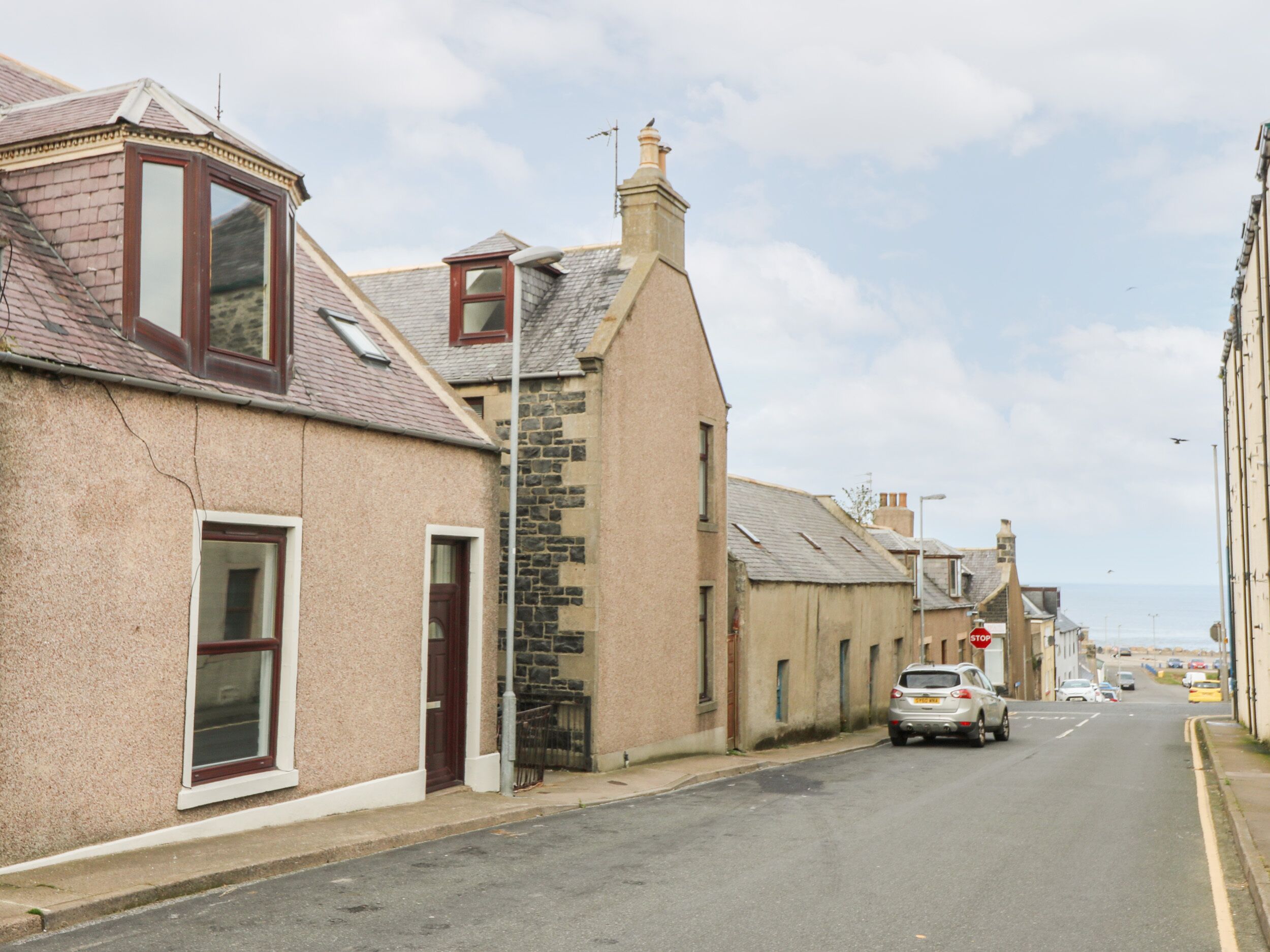 A street with traditional stone and brick buildings, a clear sky, and a car parked on the side.