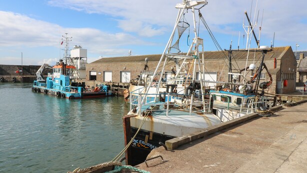A harbor with boats docked, a crane, and a building with a sign. - Rockstar Cottage (Macduff)