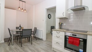A modern kitchen with a built-in oven, a dining table with chairs, and pendant lighting. - Rockstar Cottage (Macduff)