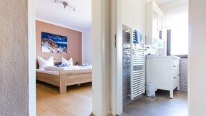 A modern hotel room with a wooden bed, a large window, a bathroom with a white sink and mirror, and a ceiling fan.