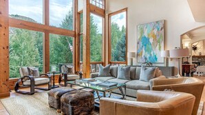 A spacious living room with large windows, a sofa set, a coffee table, and a fireplace.