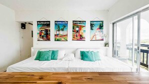 Een slaapkamer met een groot bed, kussens in teal-tint en vier kunstwerken met een thema uit Barbados.