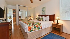Ein Hotelzimmer mit einem Bett, Nachttischen, einem Deckenventilator, einem großen Spiegel und einem Fernseher.