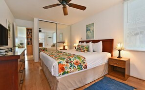 Habitación de hotel con cama, mesitas de noche, ventilador de techo, un espejo grande y televisor.
