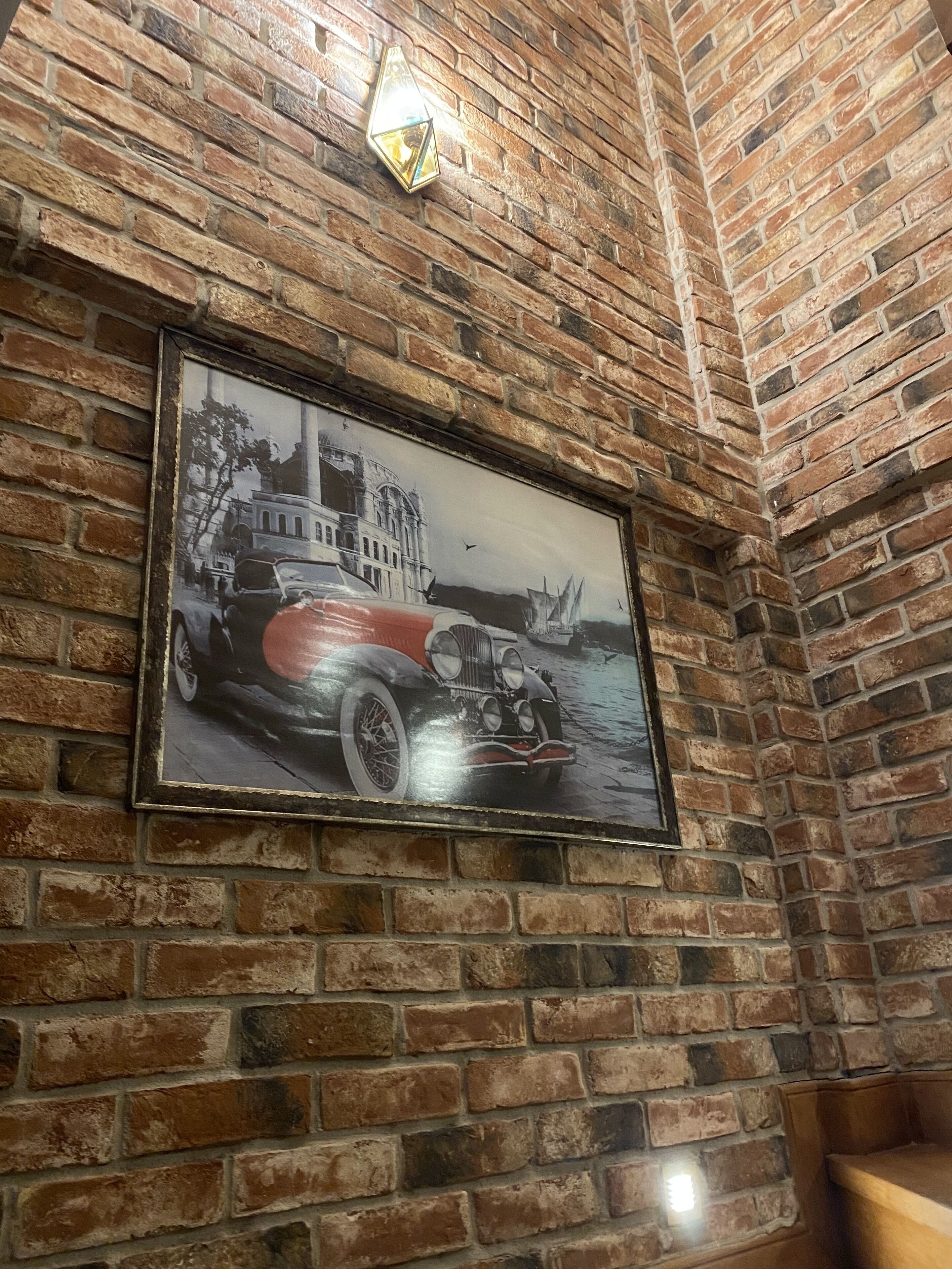 Pared de ladrillo con un cuadro enmarcado de un coche antiguo y un edificio.