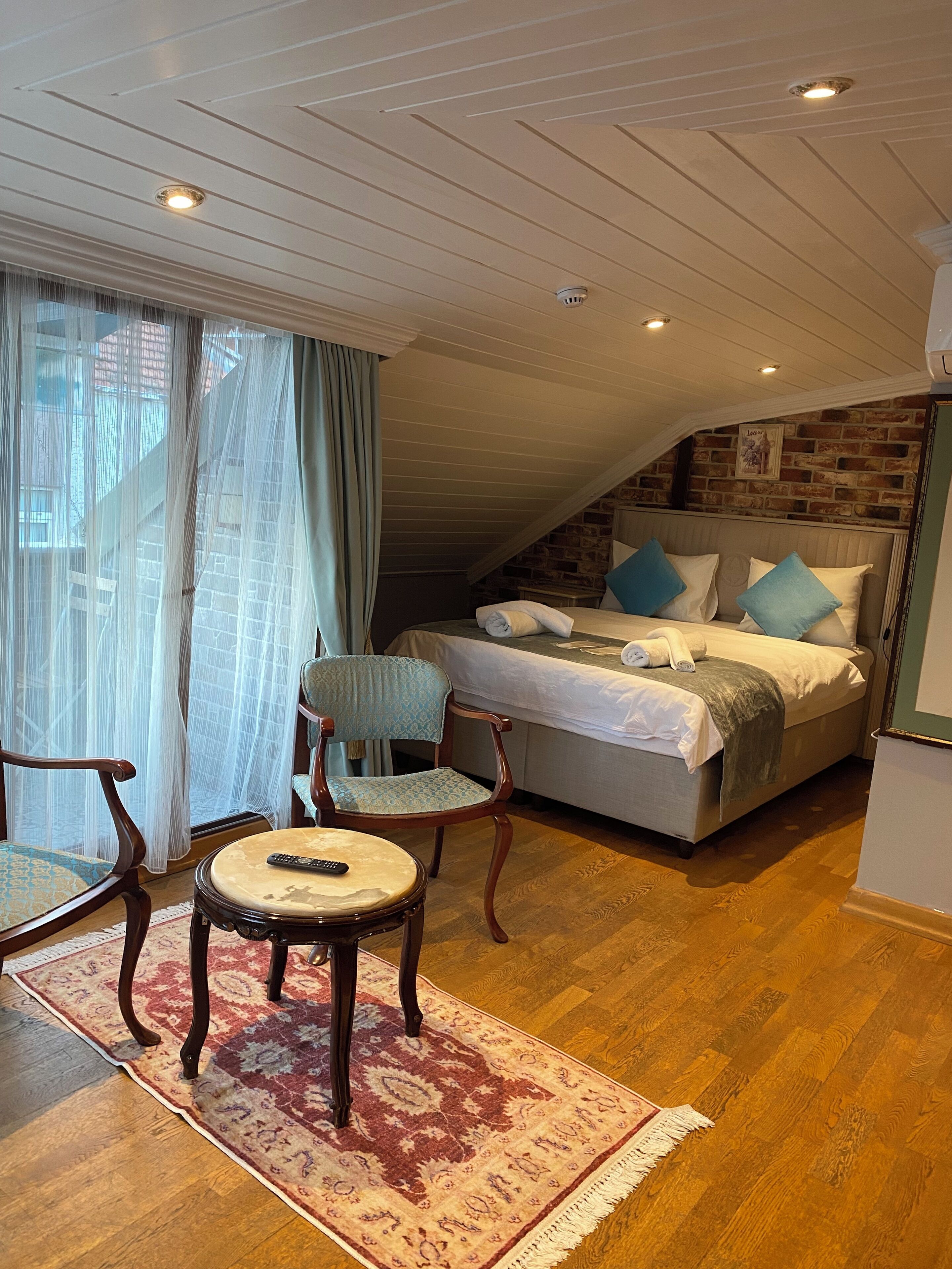 Un dormitorio con una cama grande, una silla, una mesita y una ventana con cortinas.