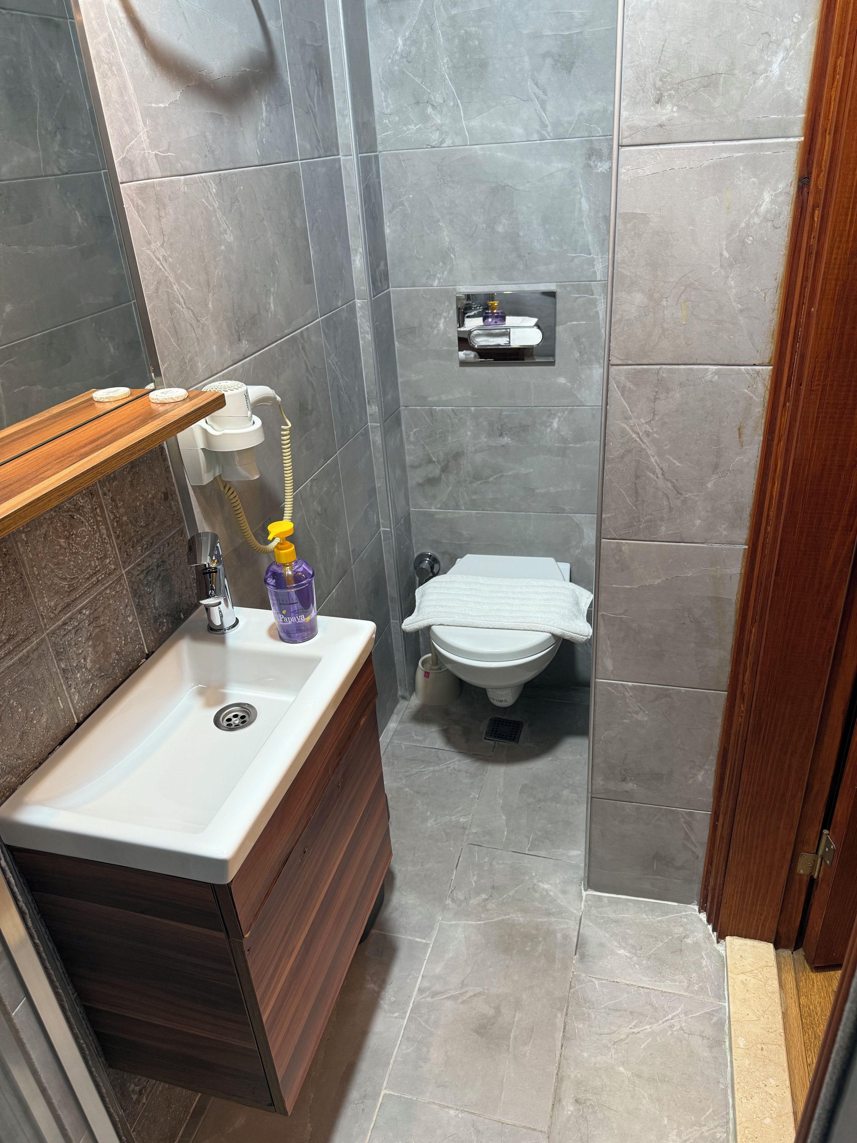 A bathroom with a wooden vanity, a white sink, a toilet, and a shower area.