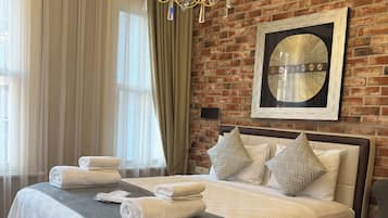 A hotel room with a large bed, a chandelier, a brick wall, and a large window with curtains.