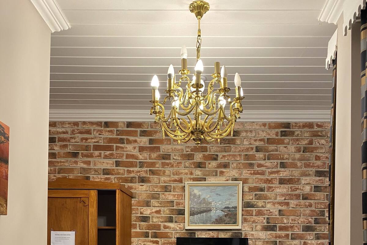 A hotel room with a brick wall, a chandelier, a television, a minibar, and a bed with towels.