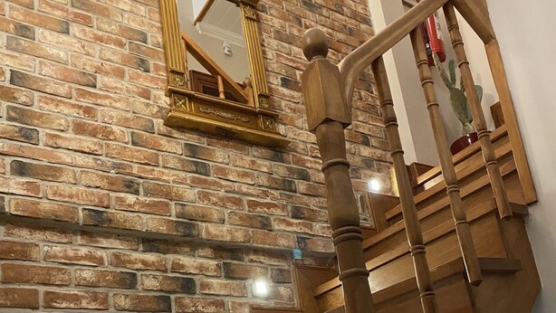 Un escalier en bois, avec un mur en briques en arrière-plan et un miroir au-dessus.