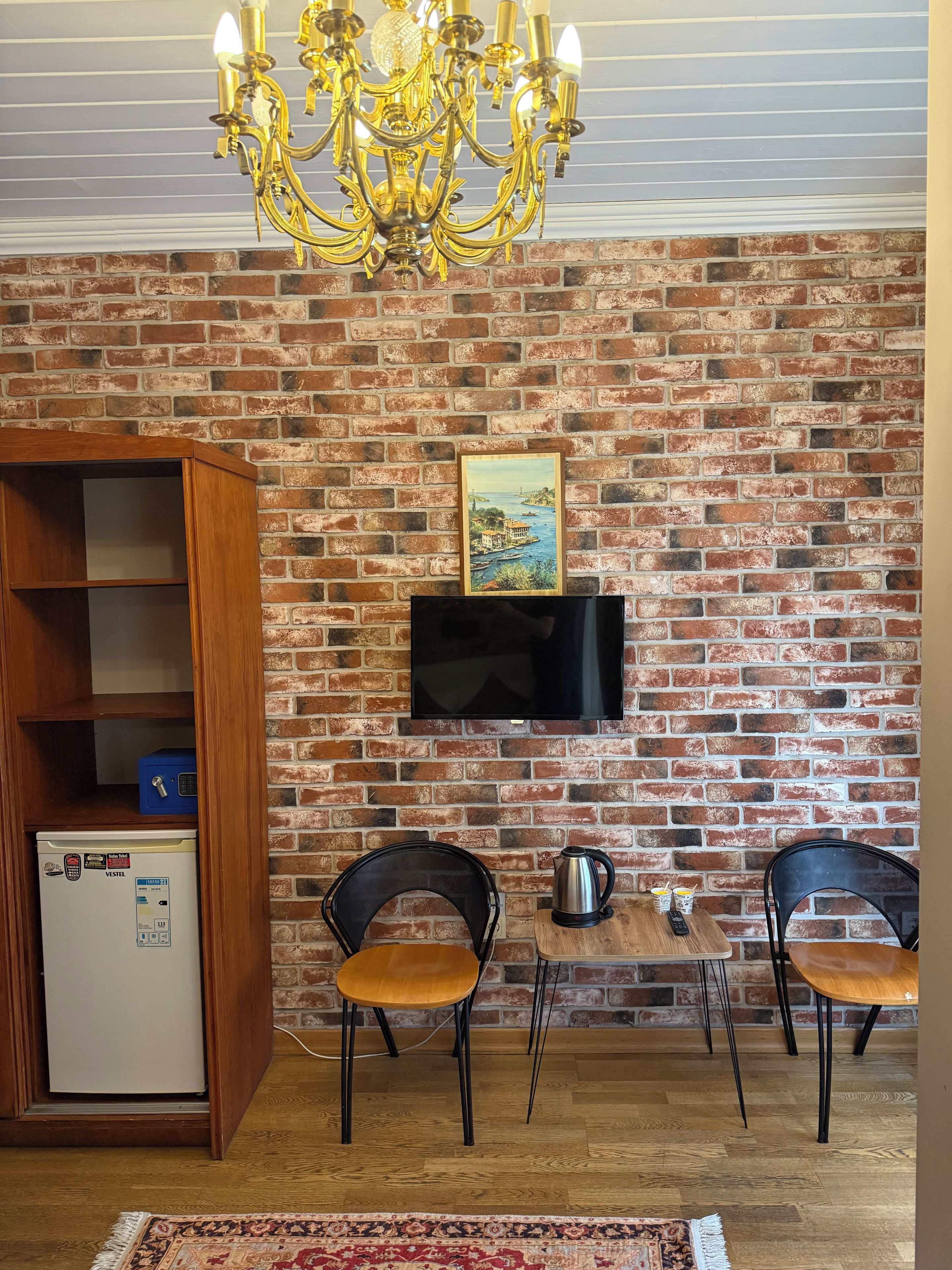 Uma sala de jantar com parede de tijolos, um candelabro, uma televisão e uma geladeira.