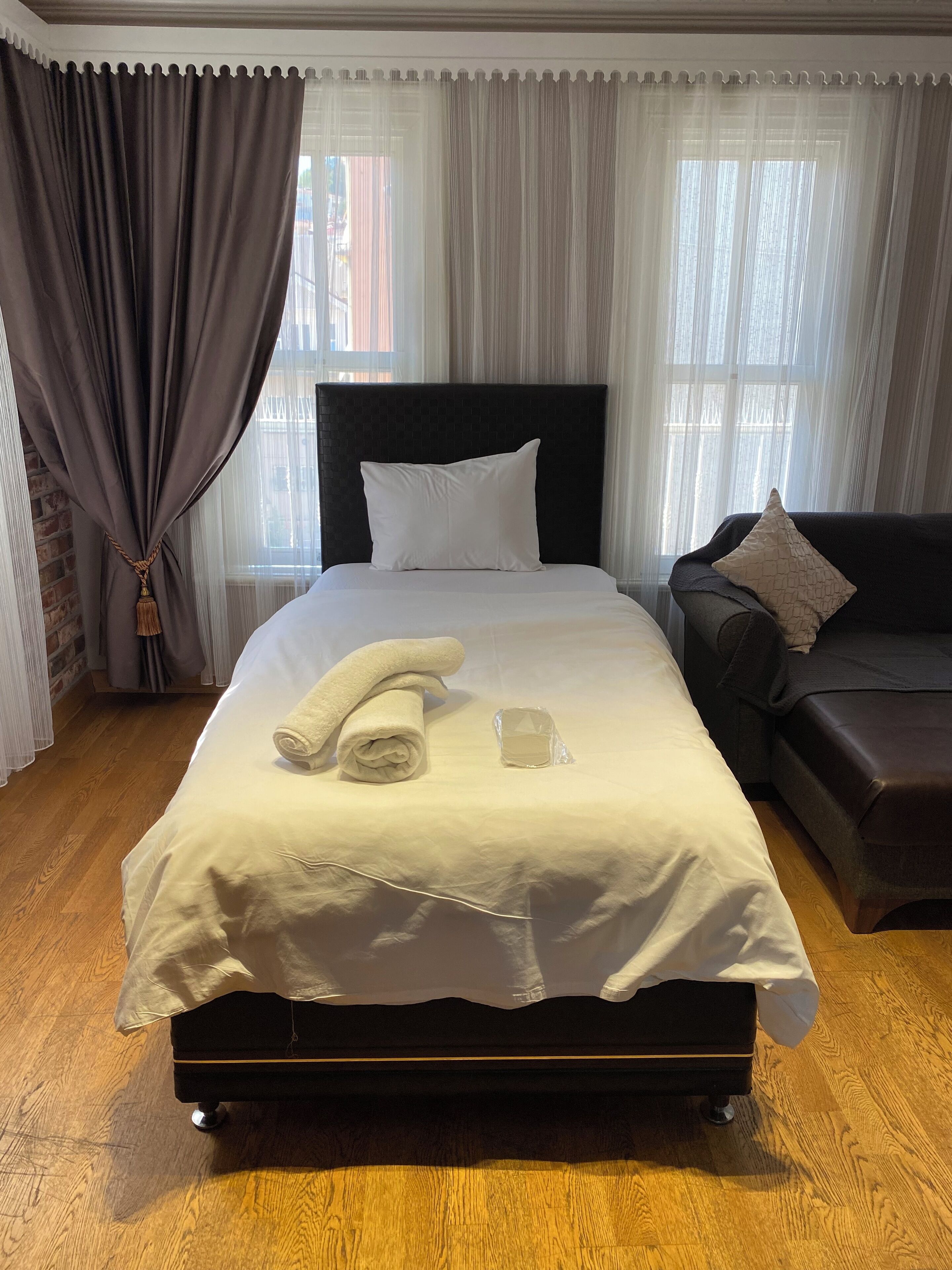 A neatly made bed with a white comforter and pillows, a rolled towel, and a glass of water on the bedside table.