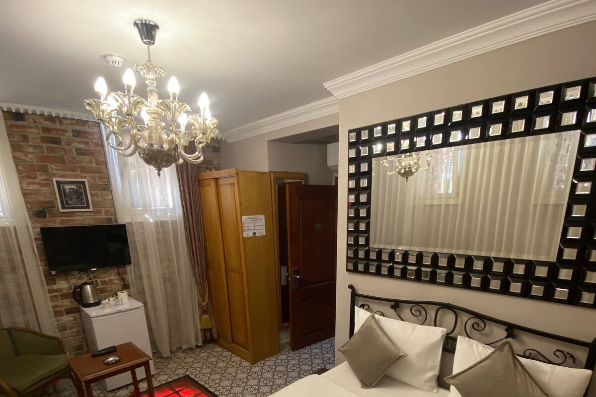 A hotel room with a bed, a TV, a wooden wardrobe, a desk, and a chandelier.