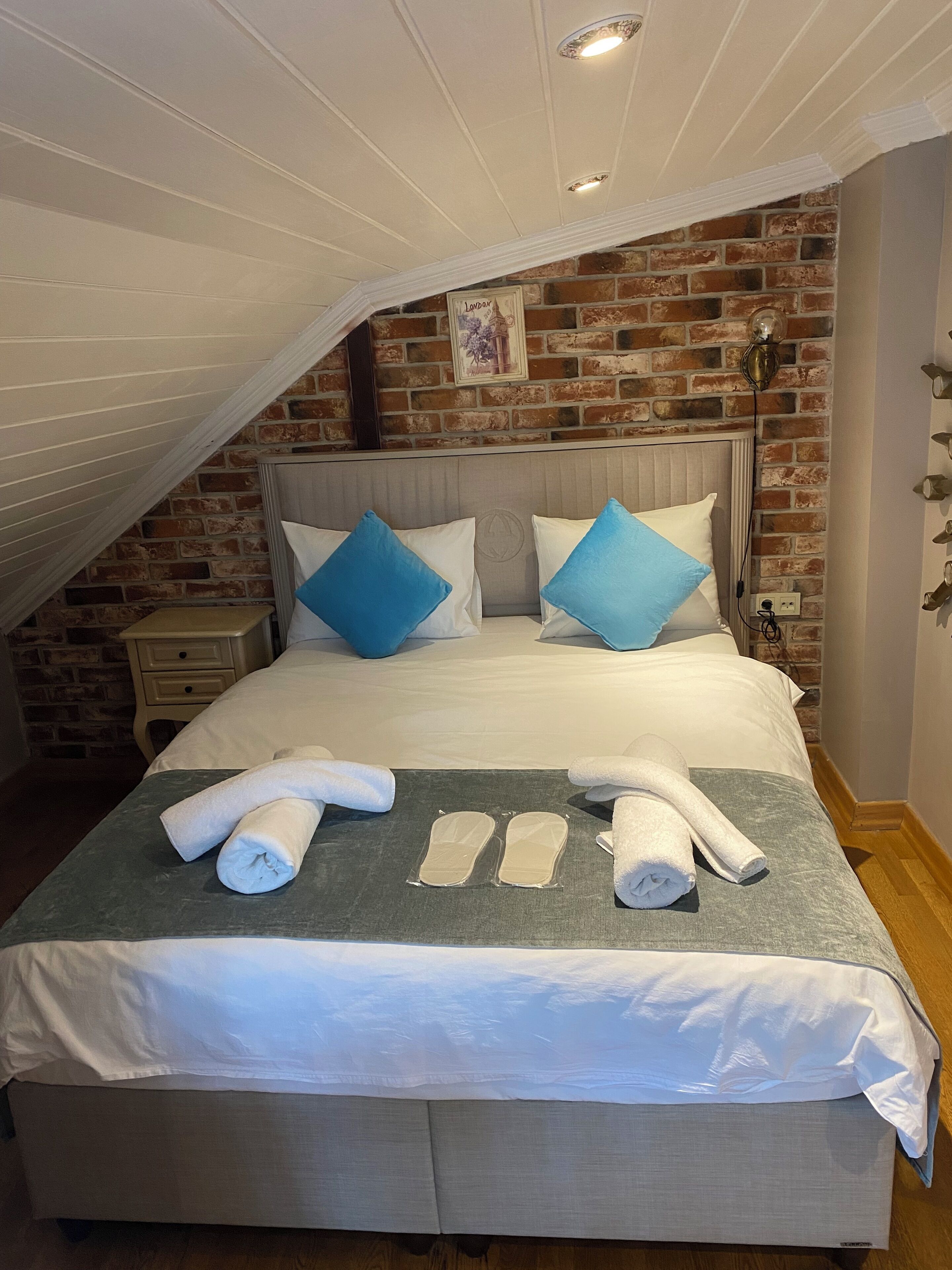 A neatly made bed with white and blue pillows, a grey blanket, and rolled towels.