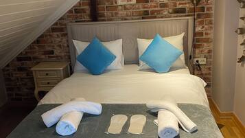 A neatly made bed with white and blue pillows, a grey blanket, and rolled towels.