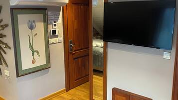 A room with wooden flooring, a framed floral artwork, a door, a mirror, and a mounted television.