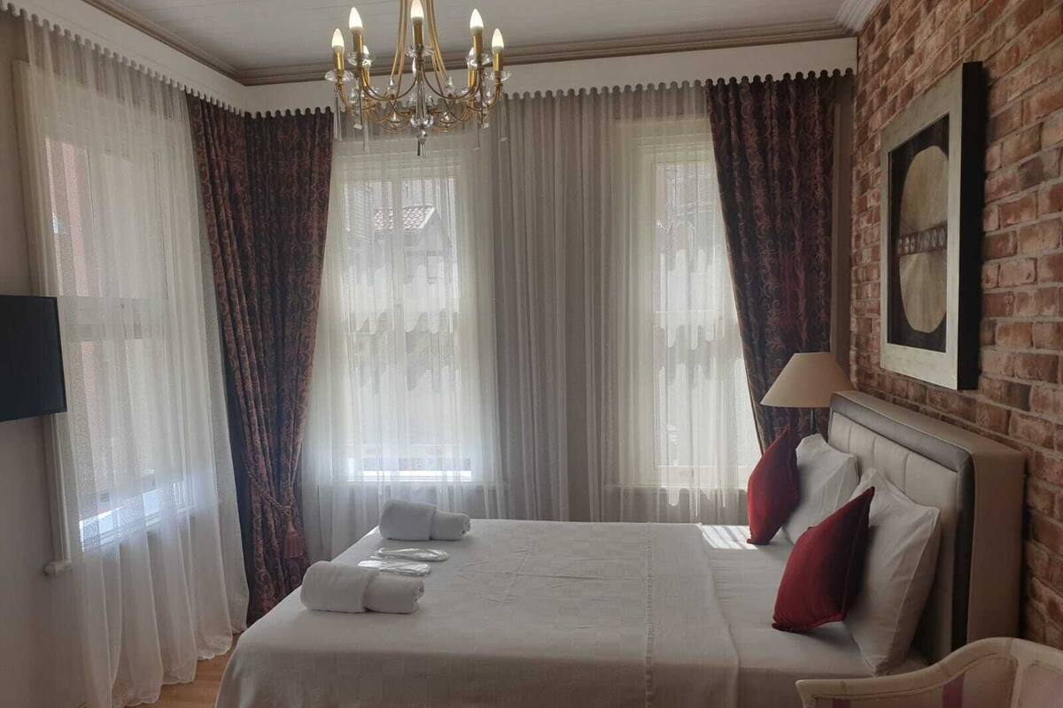 A hotel room with a bed, a chandelier, a television, and a brick wall.