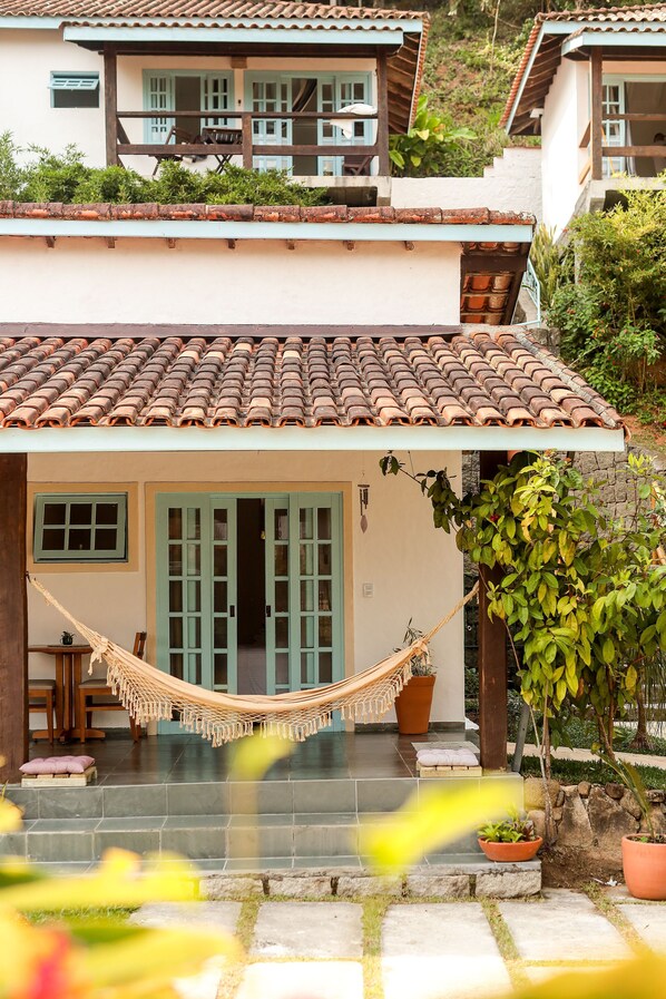 A traditional house with a tiled roof, a hammock, and potted plants.