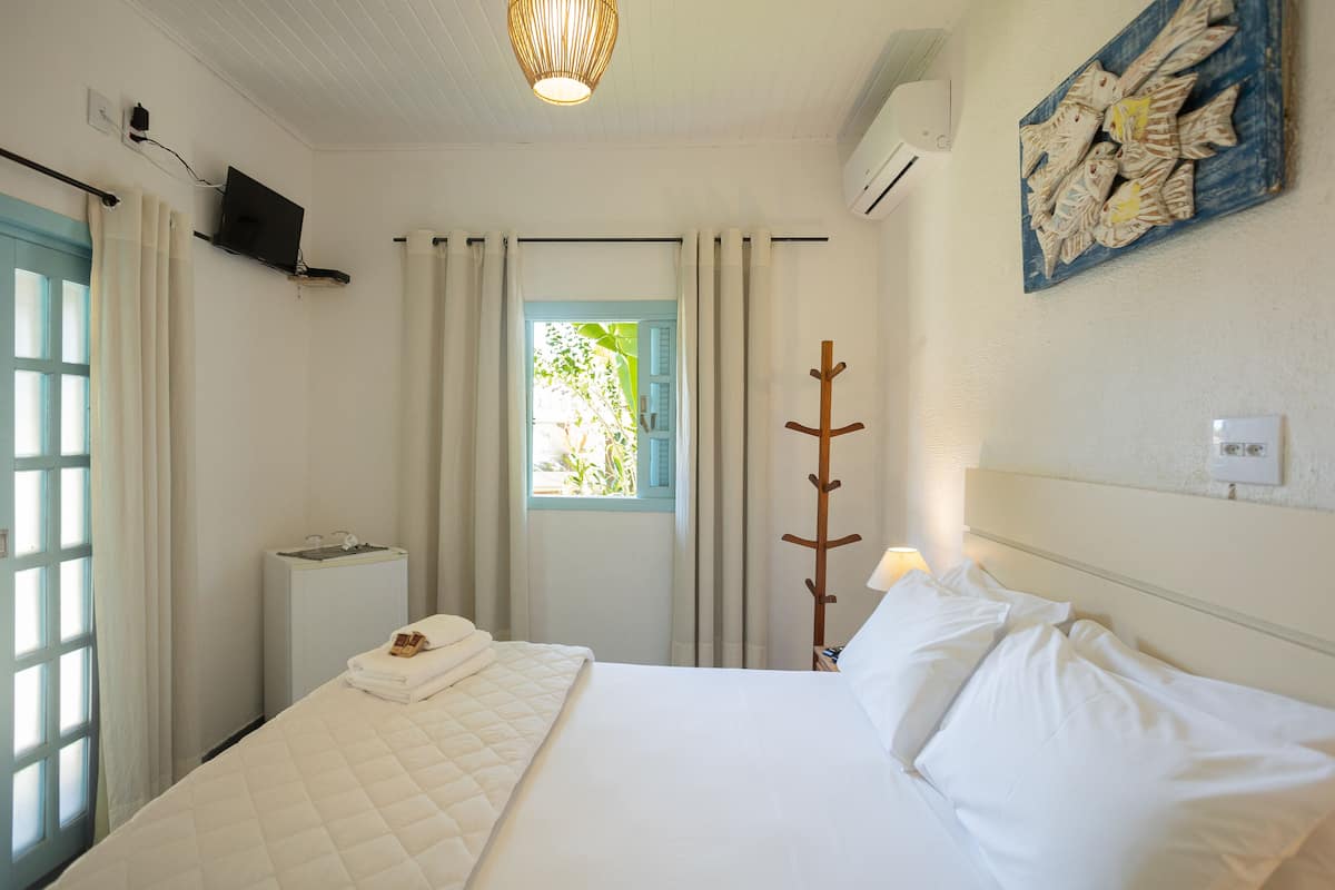 Habitación de hotel con cama, televisor montado en la pared, ventana con cortinas y perchero adherido a la pared.