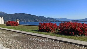 Un paseo bordeando el lago, con arbustos rojos, un camino de piedra y una vista distante de montañas y un bote en el agua.