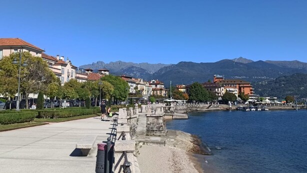 Un paseo marítimo con edificios, un puente de piedra y montañas al fondo.