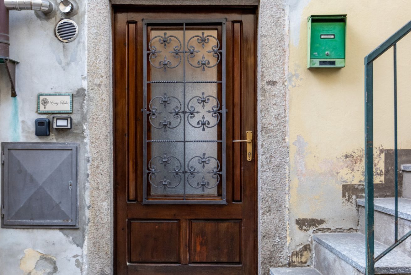 Une porte en bois avec une grille métallique, un coffret vert pour les équipements techniques et une petite plaque fixée au mur.