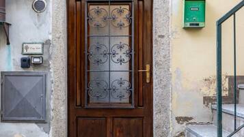 Une porte en bois avec une grille métallique, un coffret vert pour les équipements techniques et une petite plaque fixée au mur.