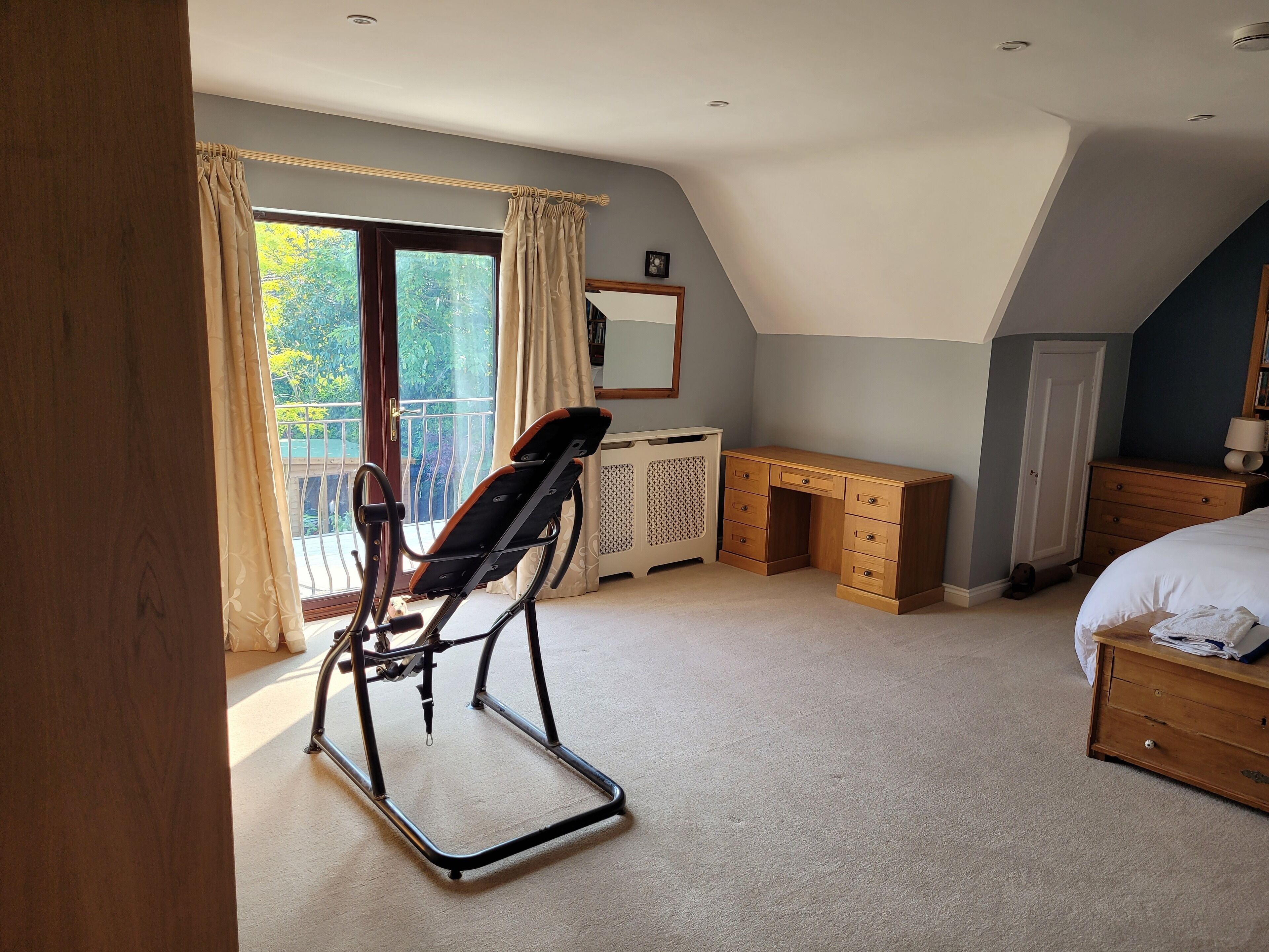 A bedroom with a bed, a desk, a chair, and a balcony.