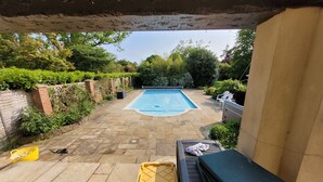 A backyard with a swimming pool, stone patio, and various outdoor furniture. - Remarkable 8 Bed Family House Sleeping 16 w/ Pool (Farnborough)
