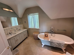 Une salle de bain avec une baignoire sur pieds, un meuble-lavabo avec un miroir et une fenêtre avec des rideaux.