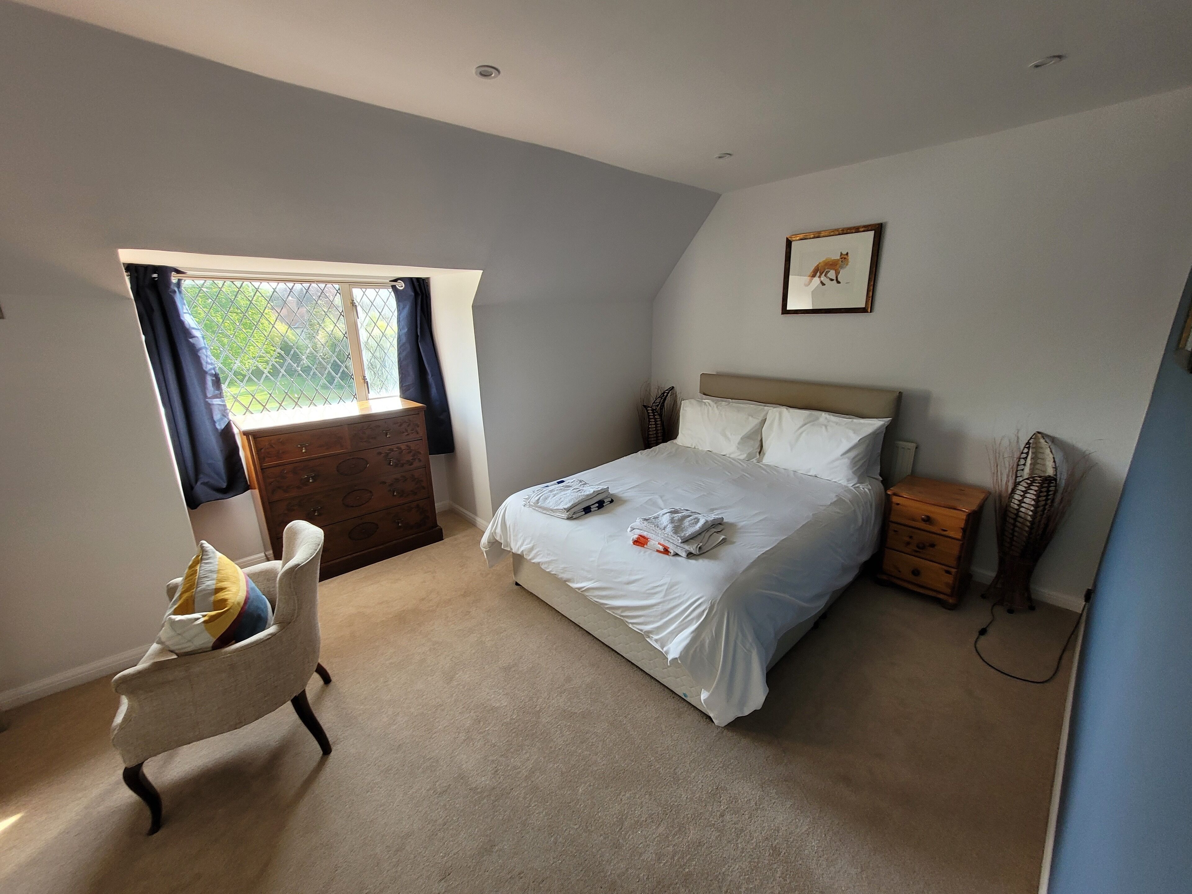 A bedroom with a bed, a chair, a dresser, and a window with curtains.