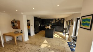 A spacious kitchen with dark cabinetry, a central island, and a dining area with a wooden table. - Remarkable 8 Bed Family House Sleeping 16 w/ Pool (Farnborough)