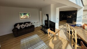 A spacious living area with a sofa, a fireplace, a dining table, and a kitchen in the background. - Remarkable 8 Bed Family House Sleeping 16 w/ Pool (Farnborough)